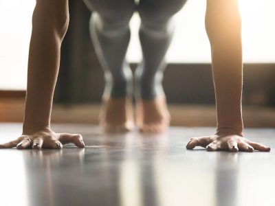 Young woman practicing yoga, doing Push ups or press ups exercise, phalankasana Plank pose, working out, wearing sportswear, grey pants, indoor, home interior, living room floor. Close-up of hands