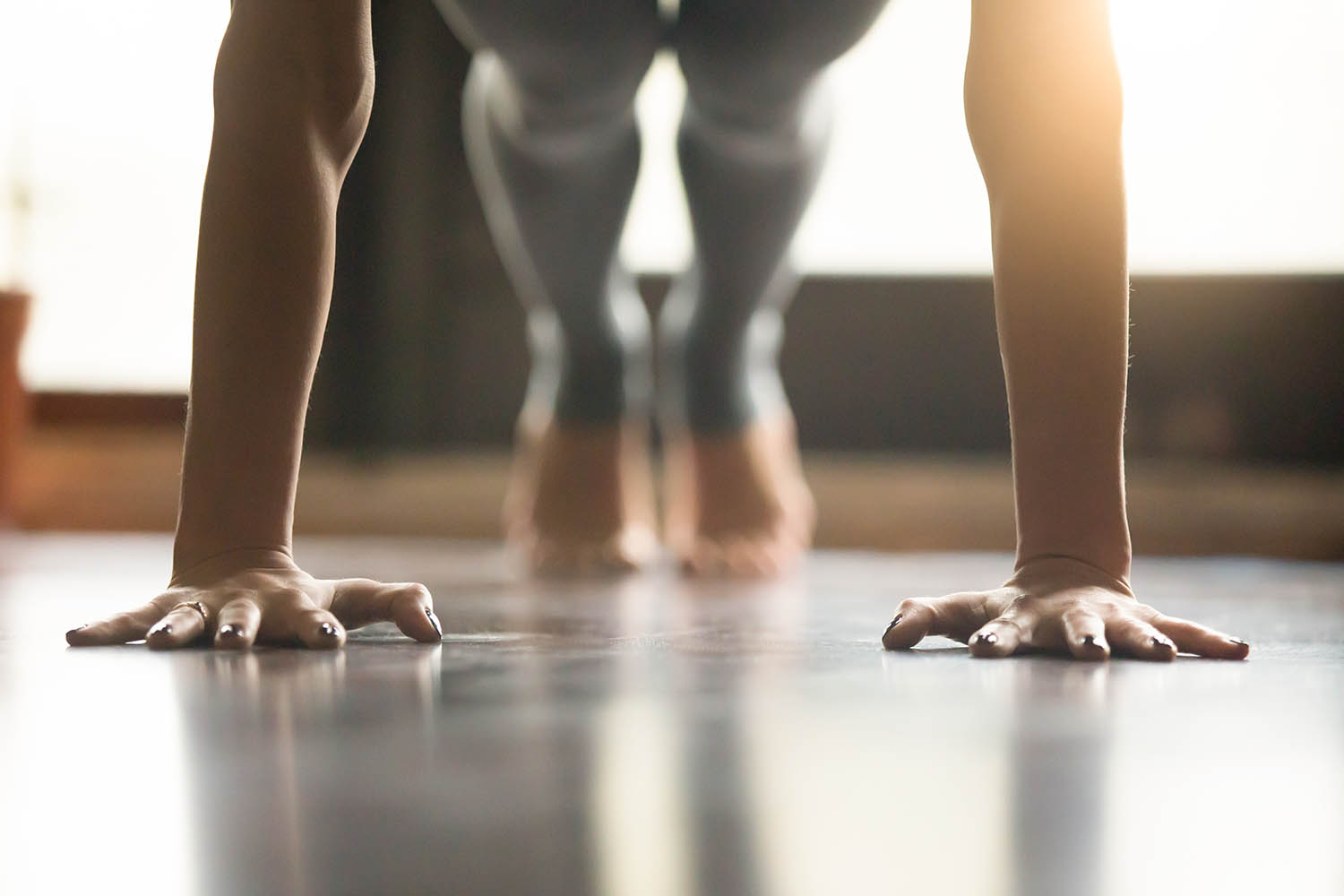 Young yogi woman standing in Plank pose, home interior backgroun Young woman practicing yoga, doing Push ups or press ups exercise, phalankasana Plank pose, working out, wearing sportswear, grey pants, indoor, home interior, living room floor. Close-up of hands